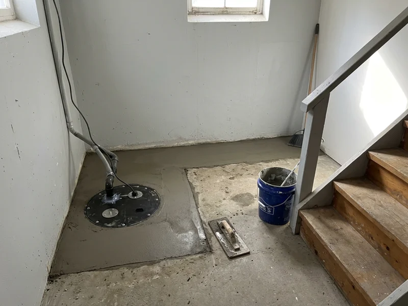 Fresh concrete re-pour along the walls with the sealed sump lid in the corner